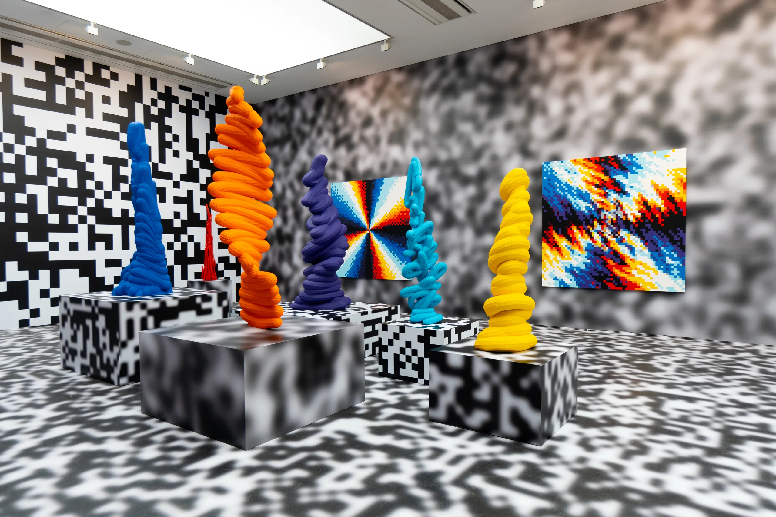 Six coiled sculptures in blue, orange, purple, cyan, red and yellow stand on blurred black-and-white plinths in a room whose floor and walls carry pixel-noise and QR patterns, with two spectral pixel paintings on the walls.